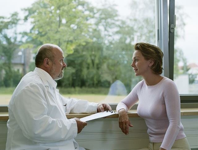 Male doctor sitting with female patient by window, side view