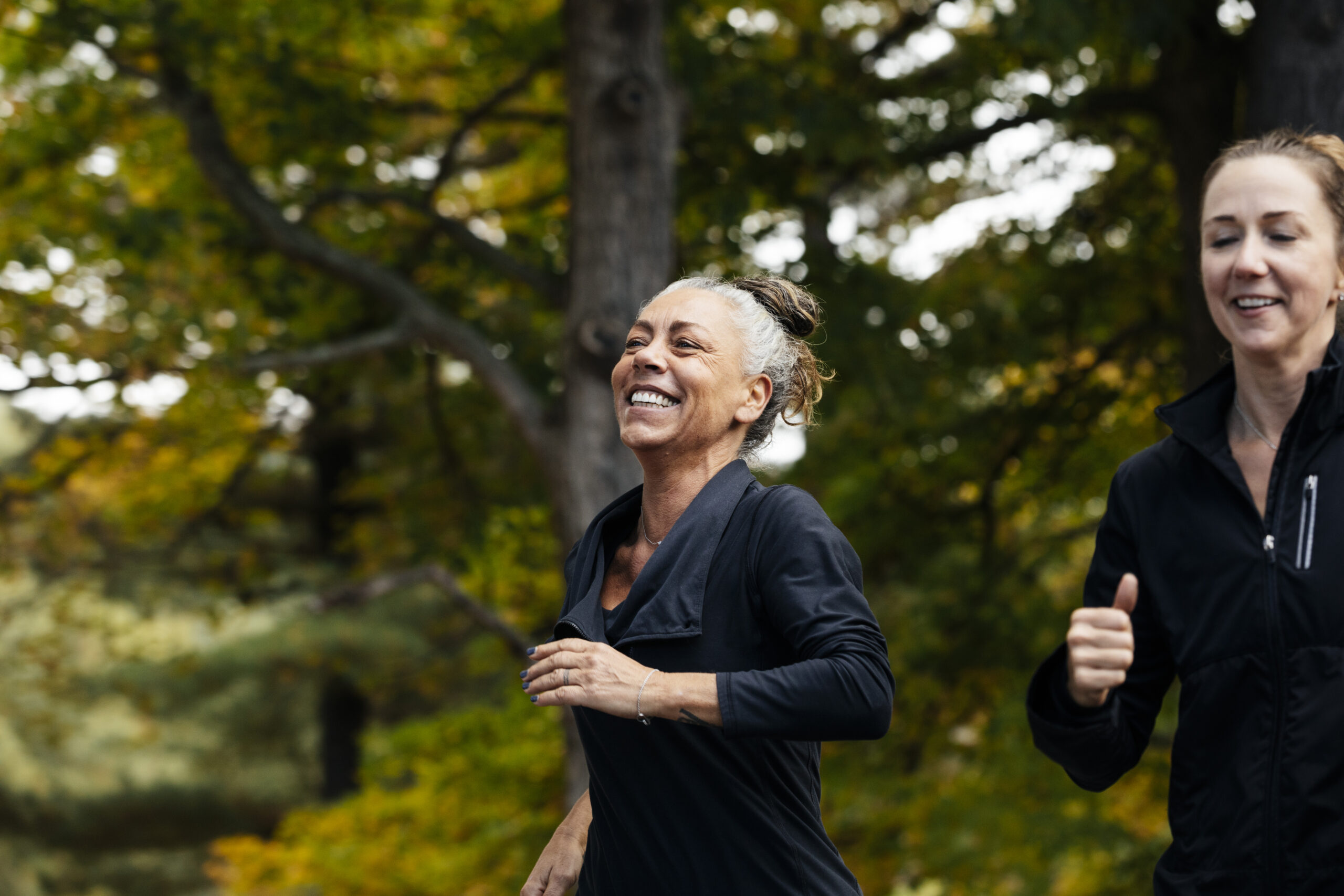 Cheerful mature woman with female friend jogging in forest